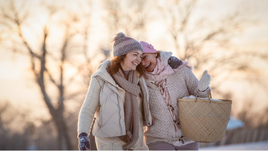 Två glada kvinnor som går i ett vinterlandskap, iklädda ullvantar och mössor.